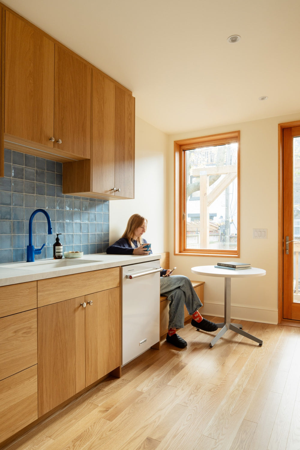 A homeowner reading at the window seat of her white oak PALET kitchen